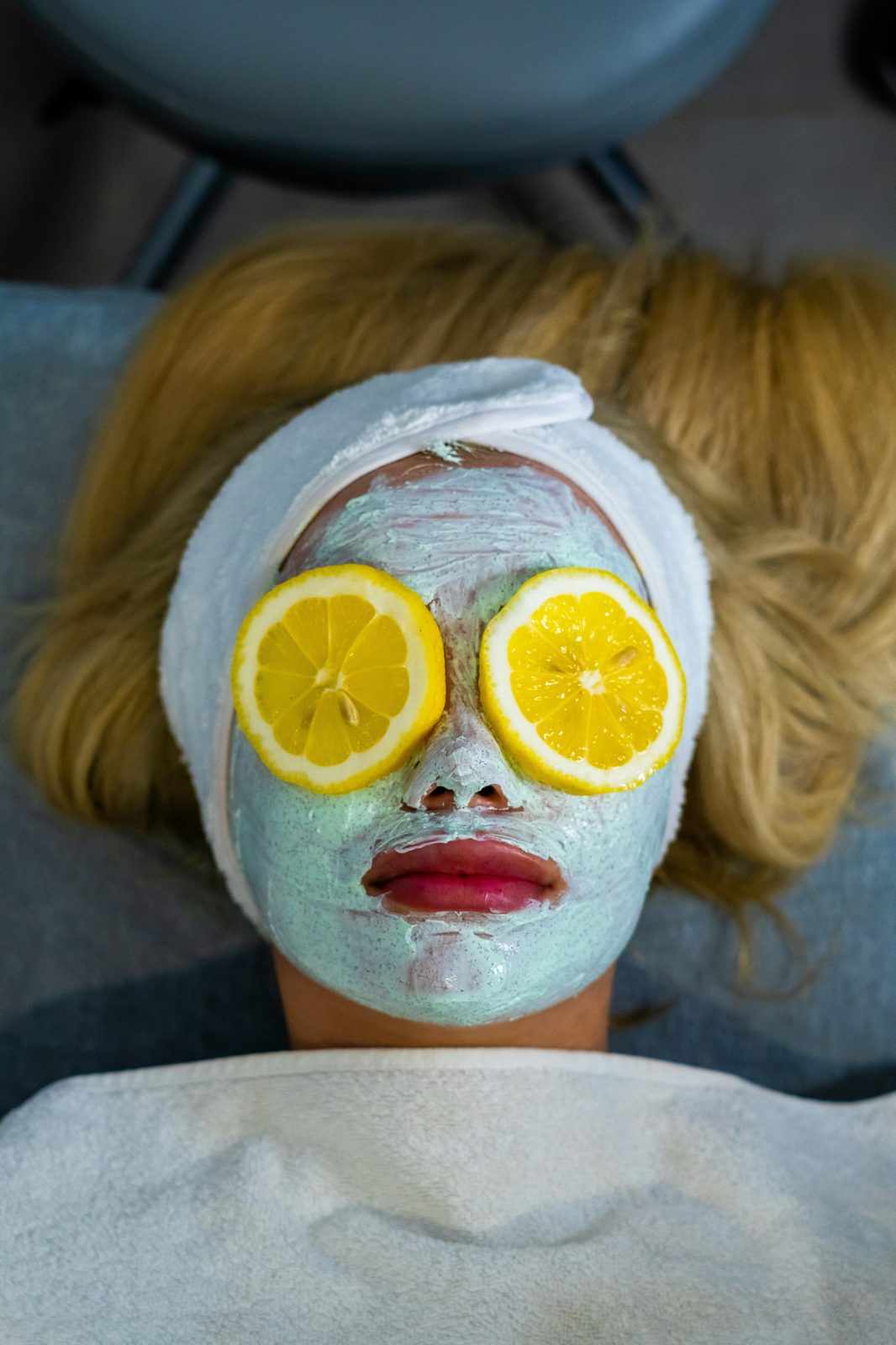 A woman with a facial mask and two lemon slices over her eyes