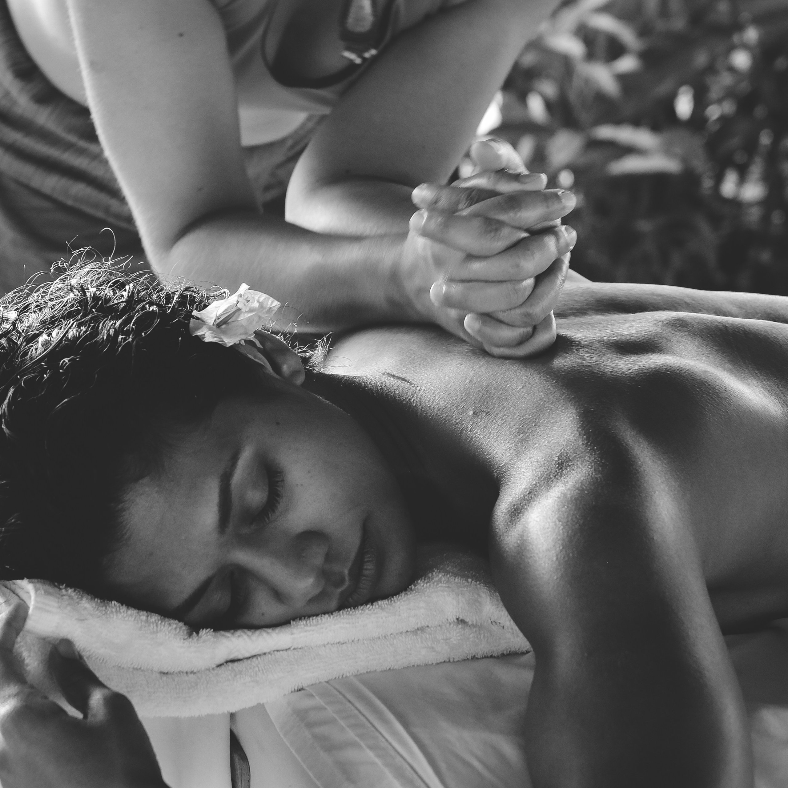 A woman receiving a slow shoulder massage, eyes closed, face resting on white linen