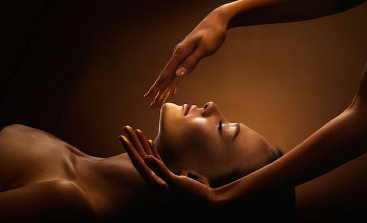 A woman lying back with eyes closed, golden-lit, hands held gently above her face and head